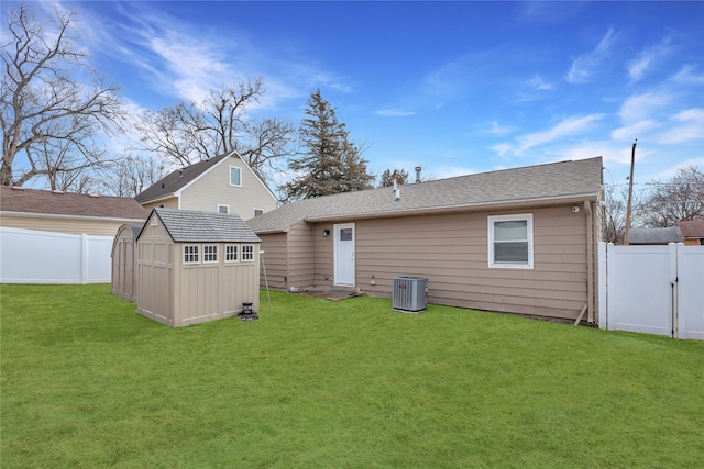 rear view of property with an outbuilding, a fenced backyard, a lawn, and central AC unit