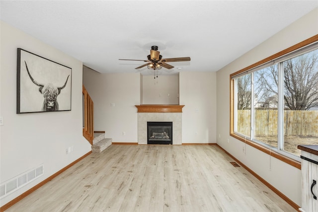 unfurnished living room featuring visible vents, baseboards, a tile fireplace, light wood-style flooring, and stairs