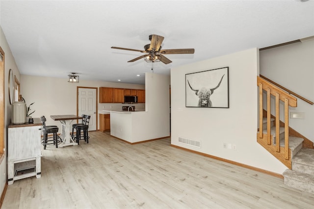 living room with ceiling fan, light wood-style flooring, visible vents, baseboards, and stairway