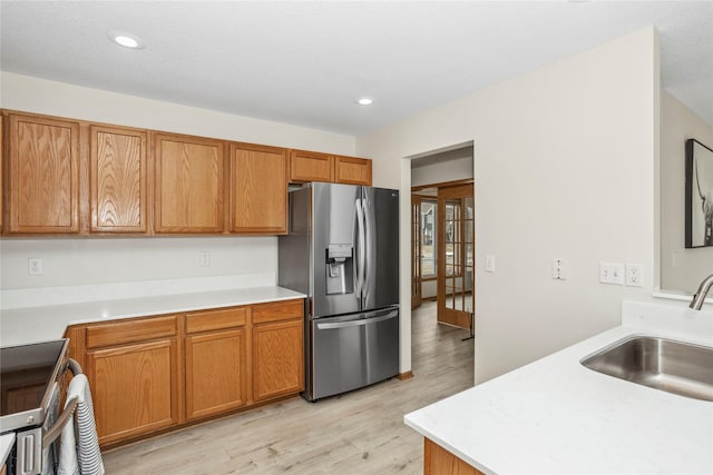 kitchen with a sink, stainless steel appliances, brown cabinetry, and light countertops