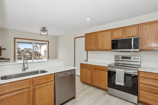 kitchen with light wood-style flooring, stainless steel appliances, a sink, light countertops, and brown cabinets