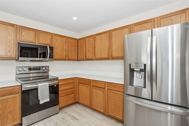 kitchen featuring stainless steel appliances, brown cabinetry, light countertops, and light wood finished floors