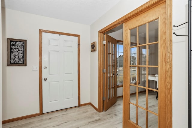 foyer entrance with light wood-style floors, french doors, and baseboards