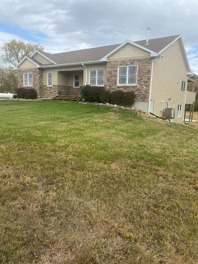 view of front of home with a front yard, stone siding, and central air condition unit