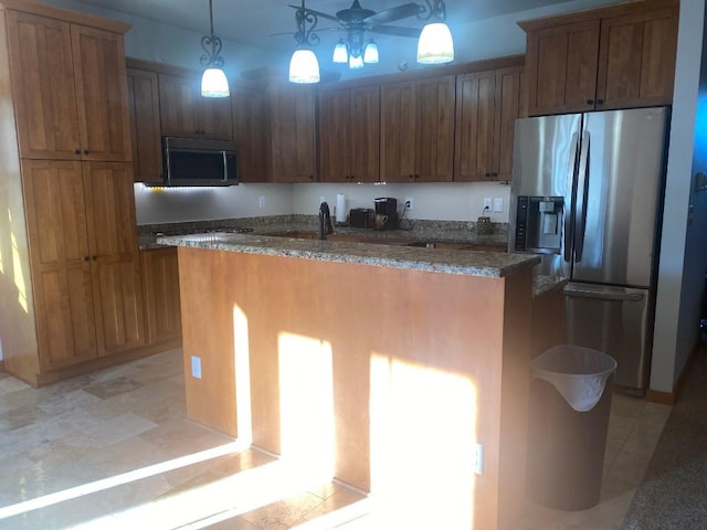 kitchen with appliances with stainless steel finishes, brown cabinets, an island with sink, dark stone countertops, and pendant lighting