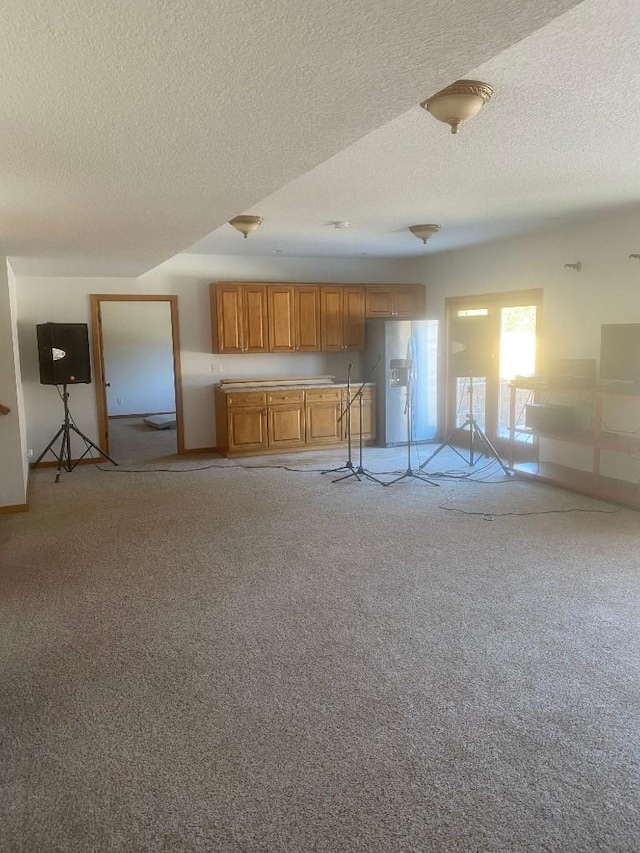 kitchen with open floor plan, white fridge with ice dispenser, a textured ceiling, and light colored carpet