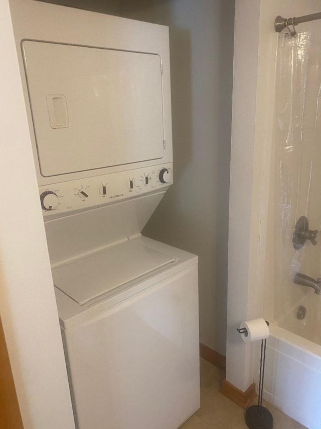 washroom featuring stacked washing maching and dryer, baseboards, light tile patterned floors, and laundry area