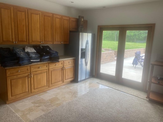 kitchen with brown cabinetry, stainless steel fridge, and dark stone countertops