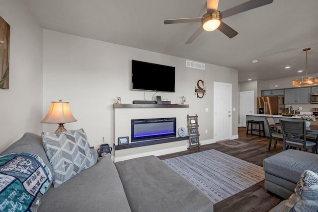 living area featuring ceiling fan, dark wood-style flooring, visible vents, baseboards, and a glass covered fireplace