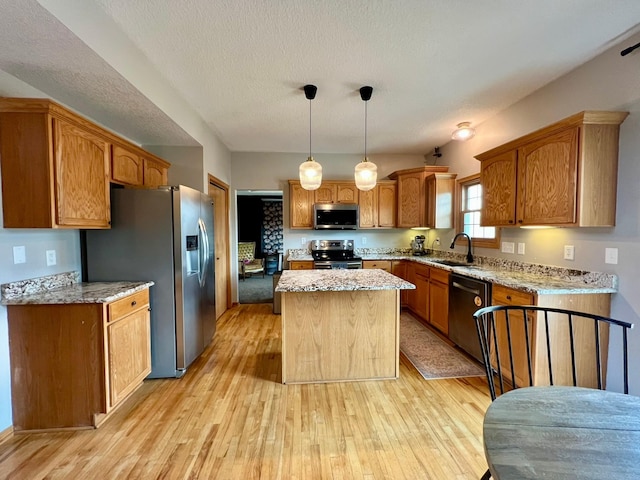 kitchen with stainless steel appliances, a sink, a center island, light wood-style floors, and light stone countertops