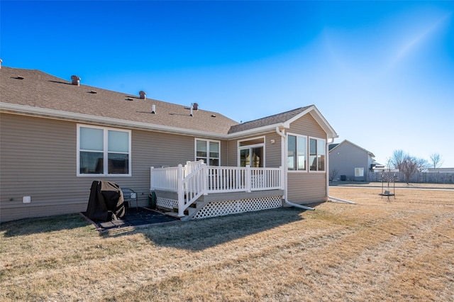 rear view of house with a deck, a shingled roof, and a lawn