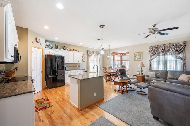 kitchen with pendant lighting, stainless steel microwave, freestanding refrigerator, open floor plan, and white cabinetry