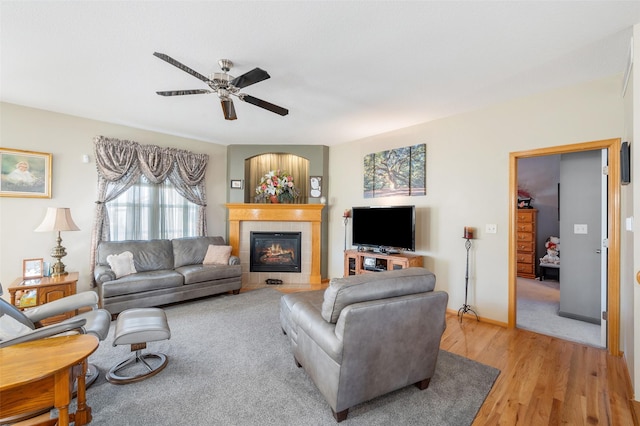 living room featuring light wood-type flooring, a tile fireplace, baseboards, and a ceiling fan