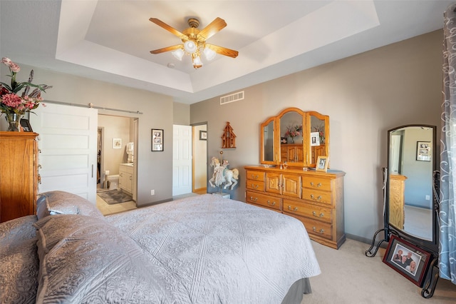 bedroom with a barn door, connected bathroom, visible vents, baseboards, and a tray ceiling