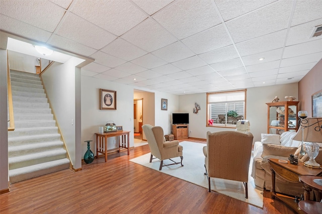 living area with a paneled ceiling, wood finished floors, visible vents, and stairs