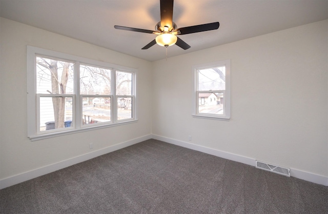 empty room featuring dark colored carpet, plenty of natural light, visible vents, and baseboards