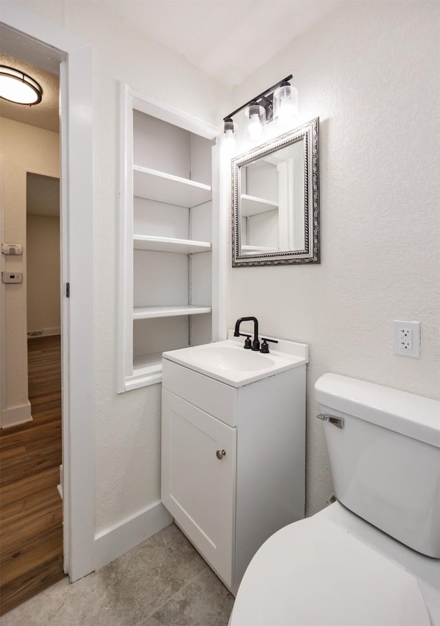 bathroom with baseboards, a textured wall, vanity, and toilet