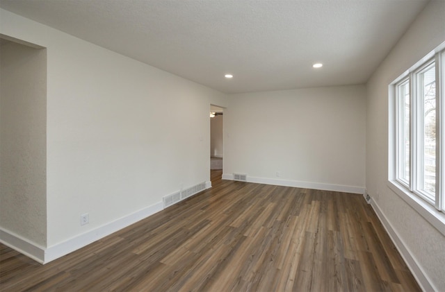 spare room featuring a wealth of natural light, dark wood-style flooring, visible vents, and baseboards