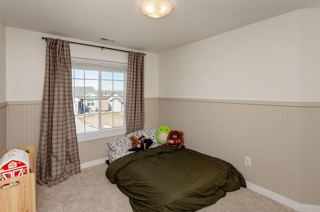 bedroom with light carpet, a textured ceiling, wainscoting, and visible vents