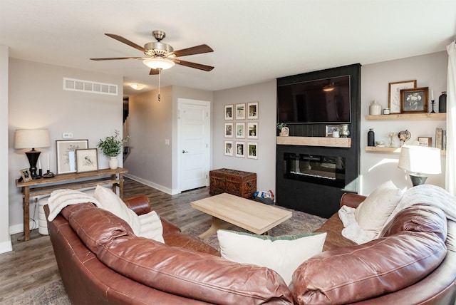 living room featuring visible vents, a fireplace, baseboards, and wood finished floors