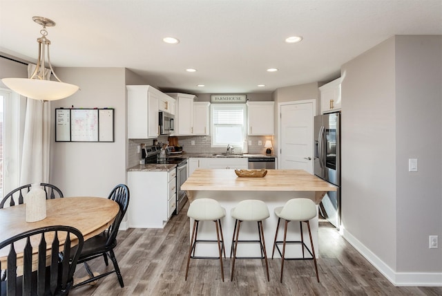 kitchen featuring stainless steel appliances, hanging light fixtures, decorative backsplash, white cabinets, and a sink