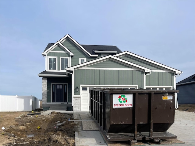 view of front facade featuring stone siding, board and batten siding, an attached garage, and fence