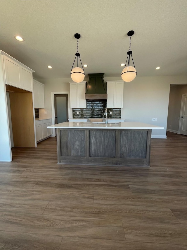 kitchen with a sink, white cabinets, decorative backsplash, an island with sink, and custom range hood