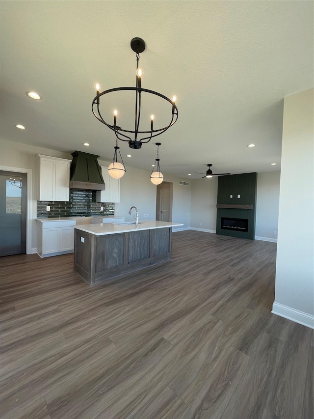 kitchen with a center island with sink, tasteful backsplash, light countertops, white cabinets, and premium range hood