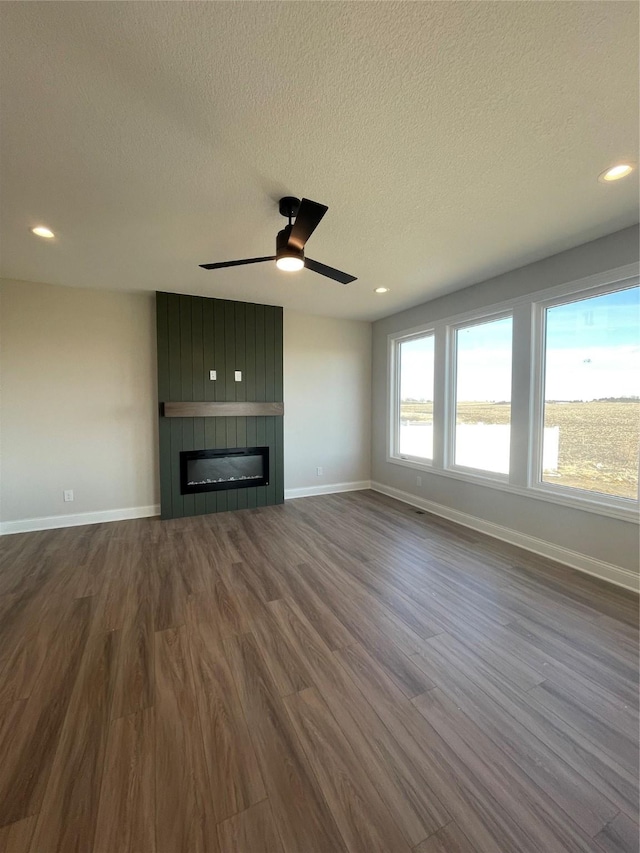 unfurnished living room with a large fireplace, baseboards, dark wood finished floors, and a textured ceiling