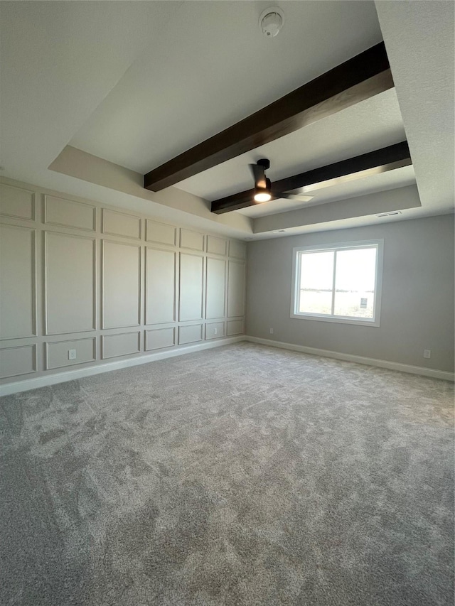 carpeted empty room featuring visible vents, baseboards, a tray ceiling, a decorative wall, and beam ceiling