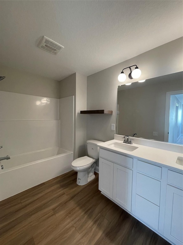 bathroom with toilet, a textured ceiling, visible vents, and wood finished floors