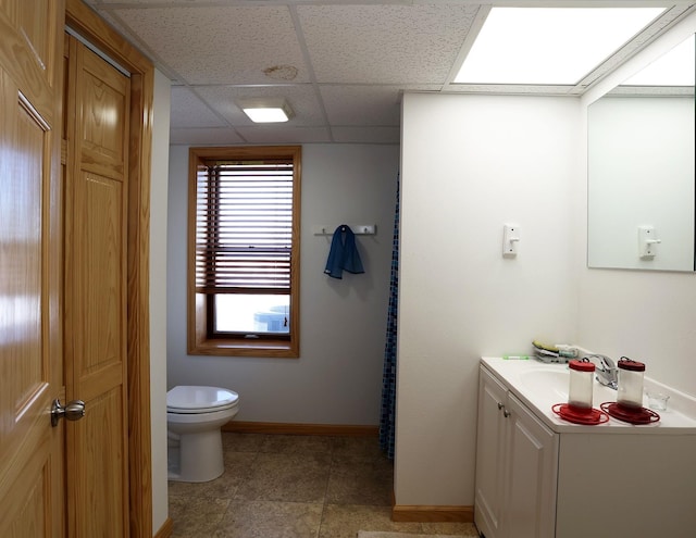 bathroom with a drop ceiling, baseboards, toilet, and vanity