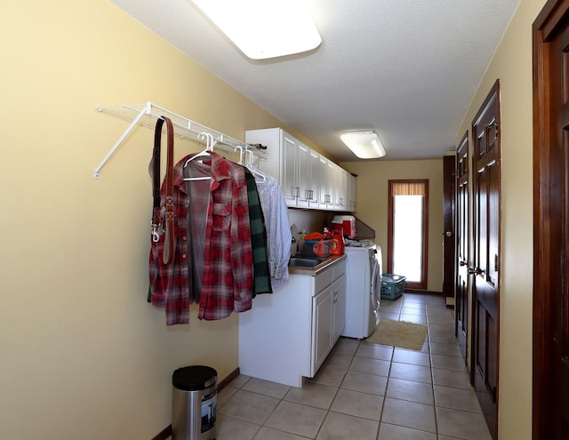 clothes washing area with light tile patterned flooring, cabinet space, a sink, a textured ceiling, and washer and clothes dryer