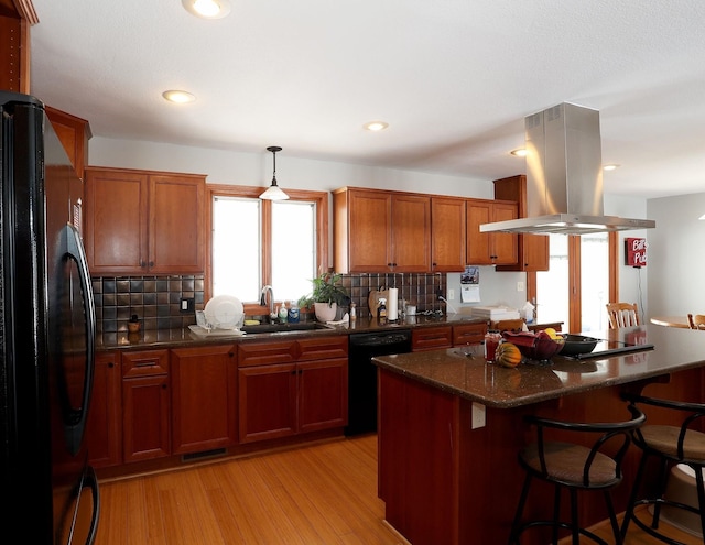 kitchen featuring a kitchen bar, black appliances, island exhaust hood, a sink, and backsplash