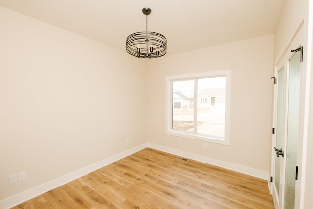 spare room featuring a notable chandelier, wood finished floors, visible vents, and baseboards