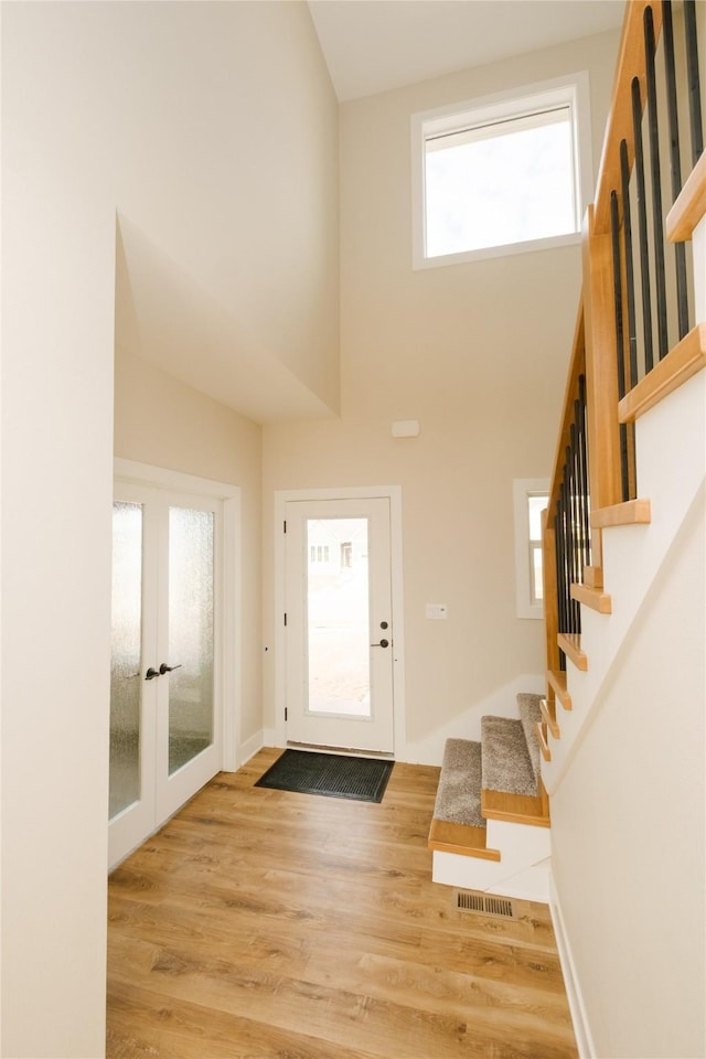 foyer entrance with french doors, visible vents, stairway, a high ceiling, and light wood-style floors