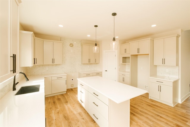 kitchen featuring light wood finished floors, light countertops, hanging light fixtures, a kitchen island, and a sink