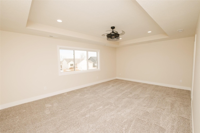 spare room featuring recessed lighting, a raised ceiling, light carpet, and baseboards