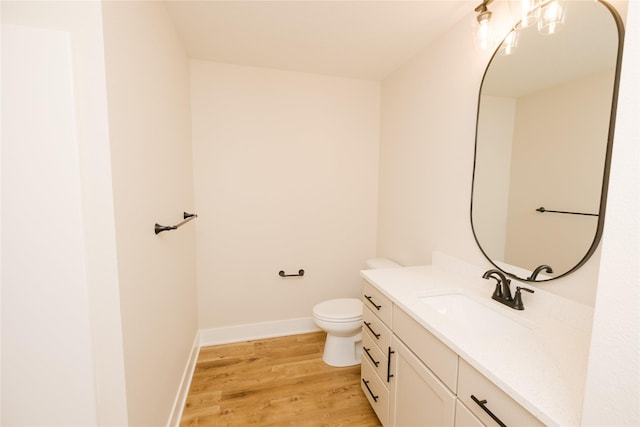 half bathroom featuring baseboards, vanity, toilet, and wood finished floors