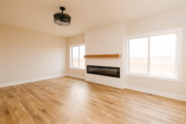 unfurnished living room featuring light wood-style floors, baseboards, and a glass covered fireplace