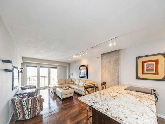 living room with dark wood-style floors, a textured ceiling, rail lighting, and baseboards