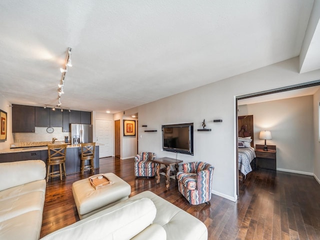 living area featuring dark wood-type flooring, rail lighting, and baseboards