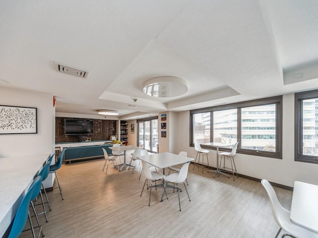 dining room with plenty of natural light, light wood-style floors, visible vents, and a tray ceiling