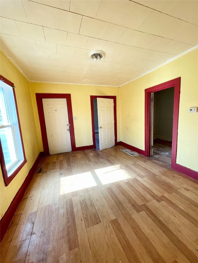 unfurnished bedroom featuring baseboards, light wood-style floors, visible vents, and crown molding