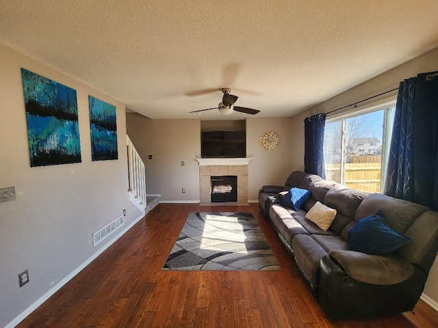 living room featuring baseboards, visible vents, a tile fireplace, dark wood-style floors, and stairway