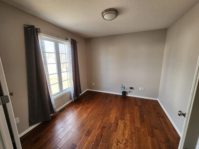 unfurnished room featuring dark wood-style flooring, visible vents, a textured ceiling, and baseboards