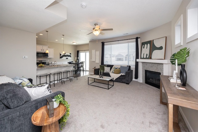 living room with light carpet, a glass covered fireplace, a ceiling fan, and recessed lighting