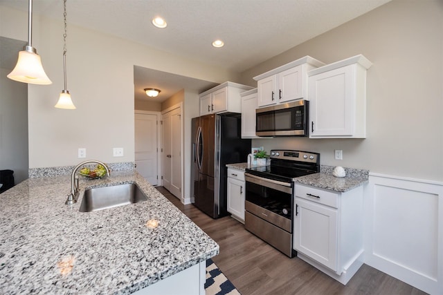 kitchen with light stone counters, hanging light fixtures, stainless steel appliances, white cabinetry, and a sink