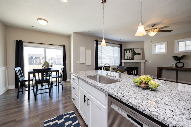 kitchen featuring decorative light fixtures, white cabinets, a sink, light stone countertops, and dishwasher