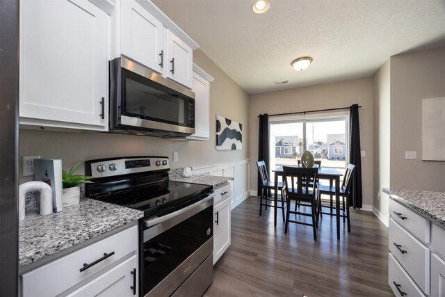 kitchen with white cabinets, dark wood-style floors, light stone countertops, stainless steel appliances, and a textured ceiling